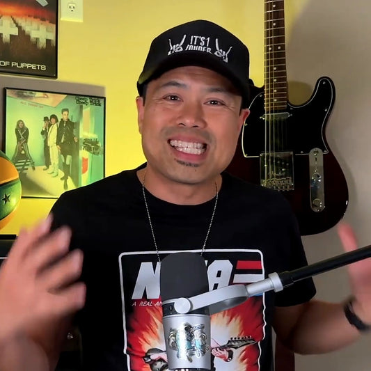 PJ Pat smiling on the It's 1 Louder podcast wearing the It's 1 Louder Black Trucker Hat with rock horns hand signs