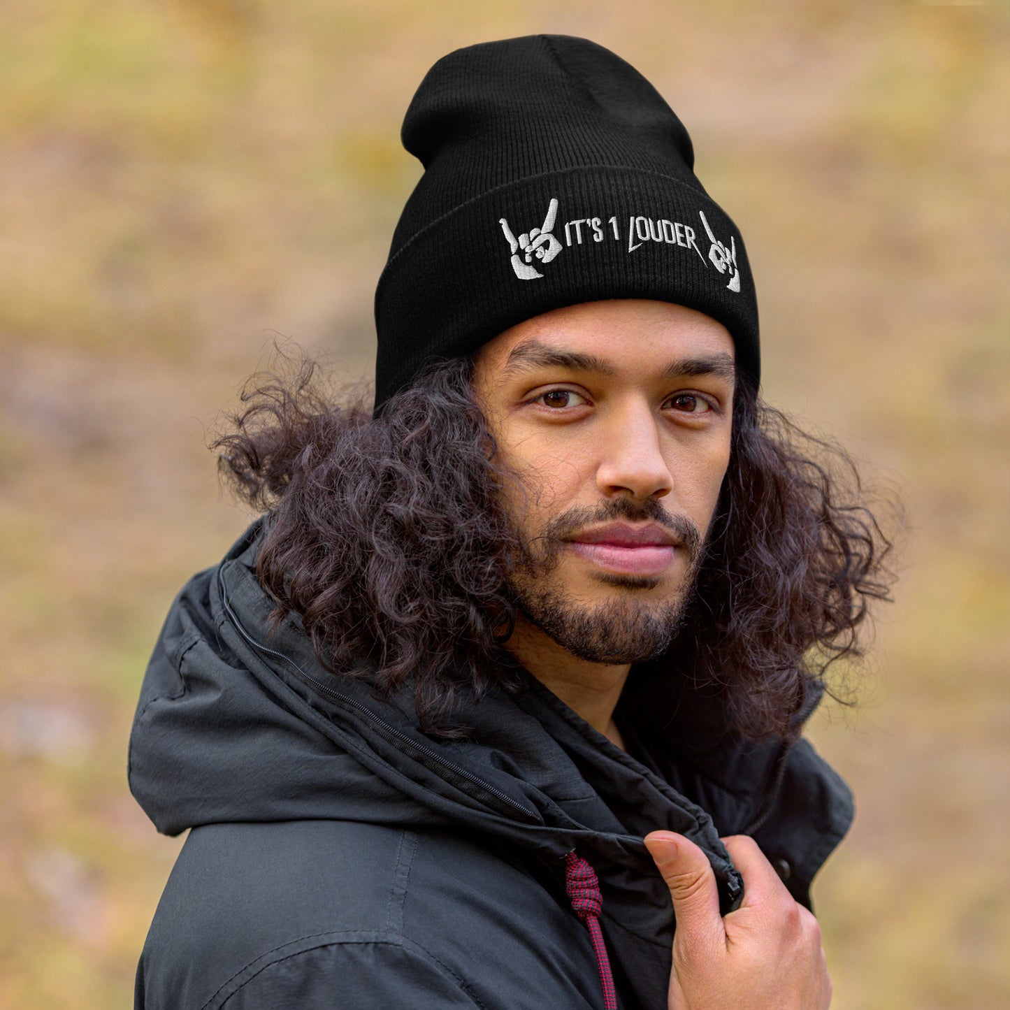 Man wearing a black beanie view front side. There are also two hands showing the rock symbol. In between those hands are the words "It's 1 Louder". The beanie would be part of a rock style or rock concert attire.