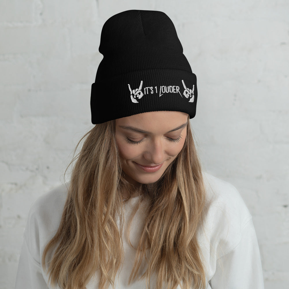 Caucasian woman wearing a black beanie view front side. There are also two hands showing the rock symbol. In between those hands are the words "It's 1 Louder". This beanie gives her a rock n roll attire or a punk rock style.