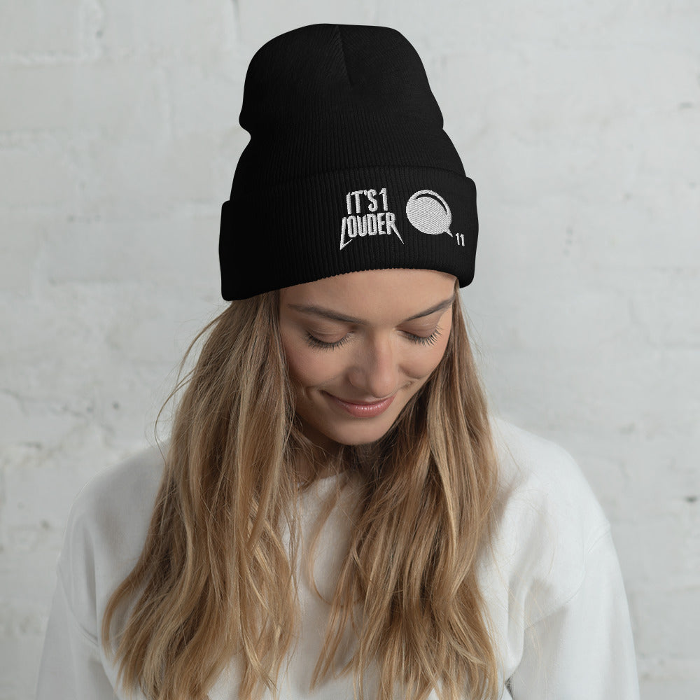 Caucasian woman wearing a black cuffed beanie. On the cuff is written on the left side the words: It's 1 Louder. On the right of this is a graphic of a volume knob from a guitar or bass amplifier pointing to 11.