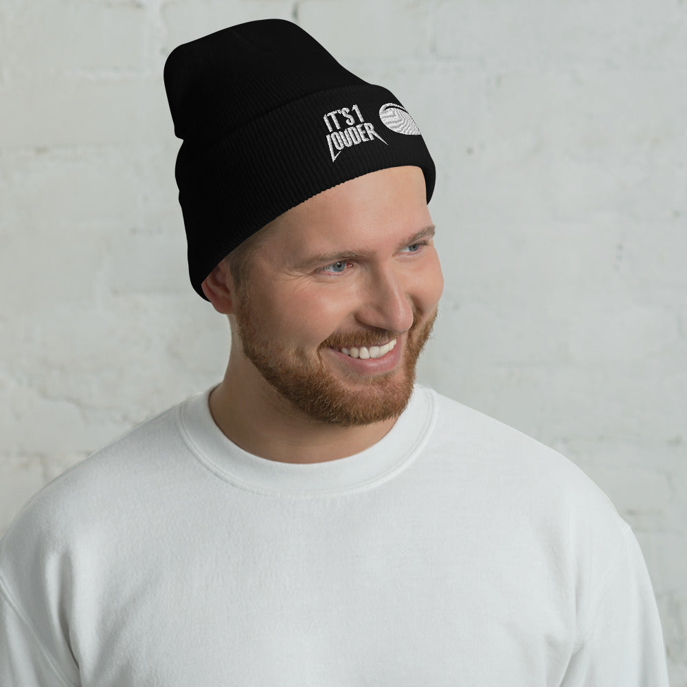 Front view of a caucasian man that is smiling and wearing a black cuffed beanie. On the cuff is written "It's 1 Louder" and beside it is a volume knob turned to number eleven. He has a punk look or rock style look. 