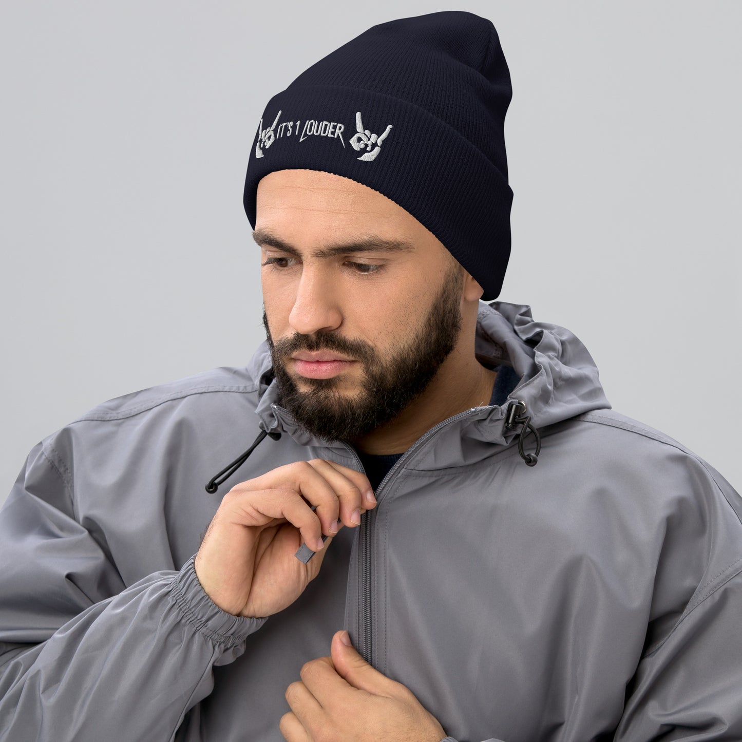 Caucasian man wearing a black beanie view front side. There are also two hands embroidered onto the beanie showing the rock & roll symbol. In between those hands are the words "It's 1 Louder". The beanie would be part of a rock style or rocker clothing.