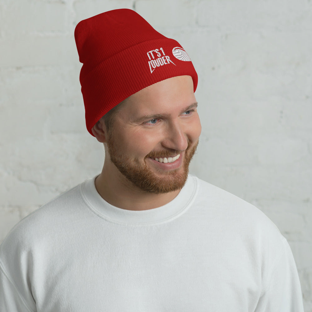 Caucasian man wearing a red cuffed beanie. On the cuff is written on the left side the words: It's 1 Louder. On the right of this is a graphic of a volume knob from a guitar or bass amplifier pointing to the number eleven.